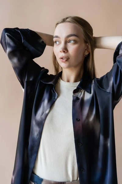 Young and trendy woman with hands behind head looking away isolated on beige — Stock Photo