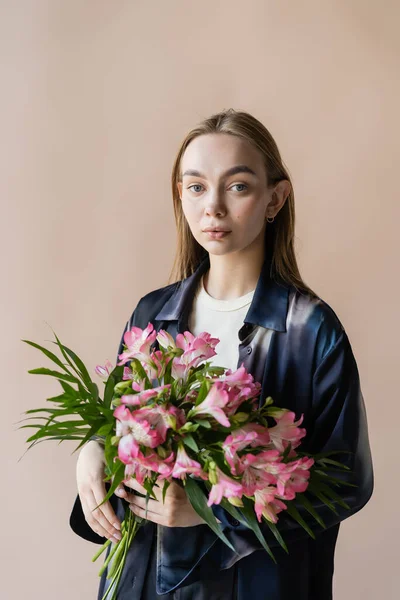 Mujer encantadora con flores de alstroemeria mirando a la cámara aislada en beige - foto de stock