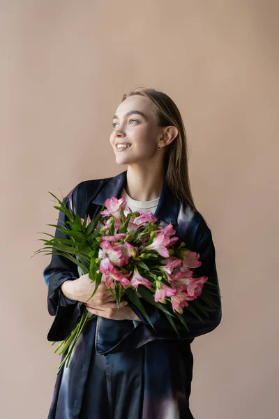 Mujer feliz y de moda con ramo floral fresco mirando hacia otro lado aislado en beige — Stock Photo