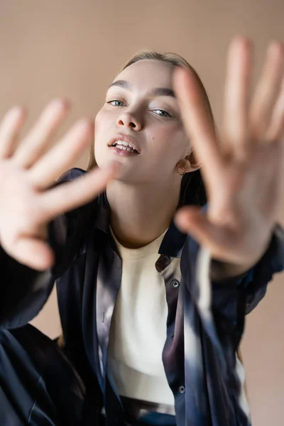 Sensual and stylish woman with blurred outstretched hands looking at camera isolated on beige - foto de stock