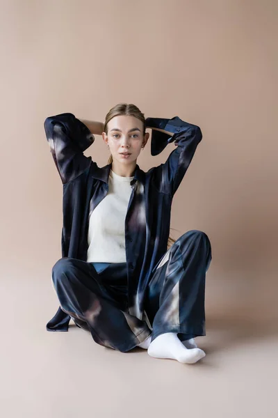 Fashionable woman sitting with hands behind head on beige background — Stockfoto