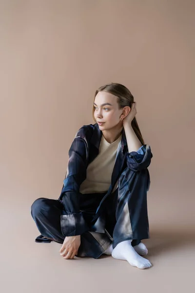 Jeune femme en costume dégradé assis et regardant loin sur fond beige — Photo de stock