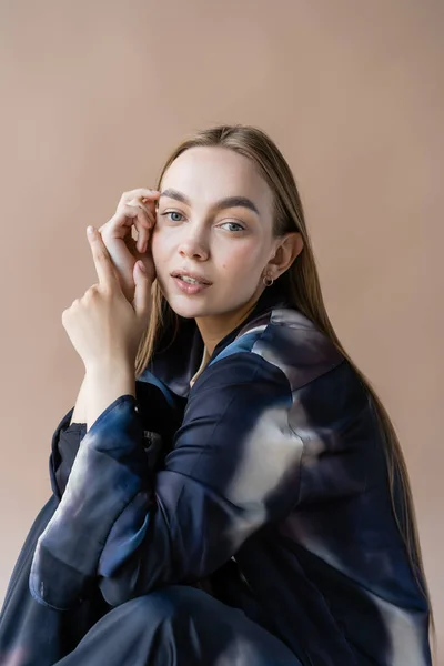 Trendy langhaarige Frau mit den Händen in der Nähe Gesicht Blick in die Kamera isoliert auf beige — Stockfoto