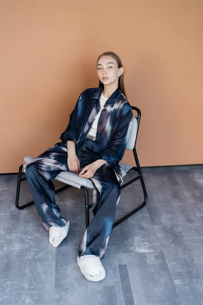 High angle view of woman in tie-dye style suit sitting on modern chair on beige background — Stock Photo