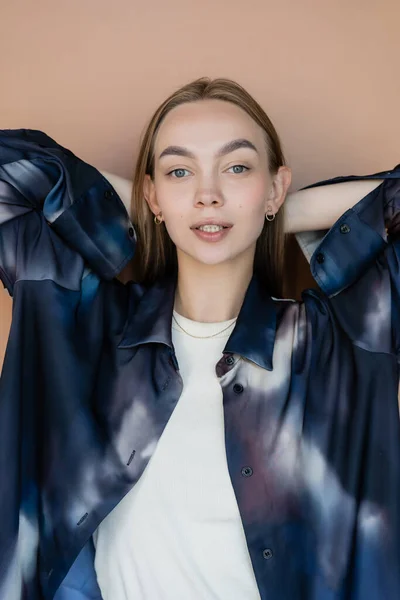 Woman in oversize gradient shirt posing with hands behind head isolated on beige - foto de stock