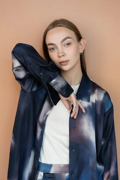 Mujer de moda en camisa de estilo tie-dye mirando a la cámara mientras posa aislado en beige - foto de stock