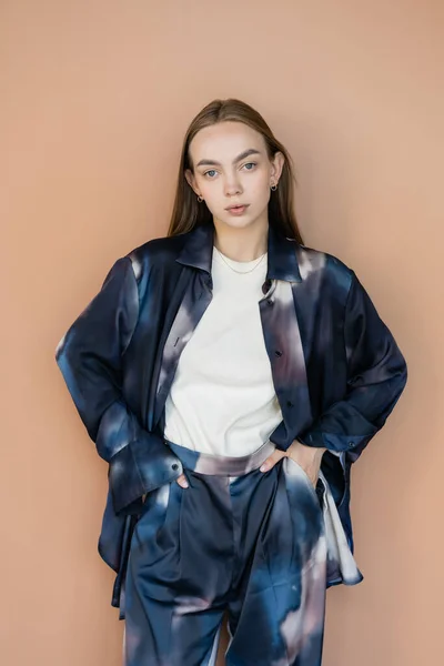 Young woman in trendy oversize suit standing with hands in pockets isolated on beige — Stock Photo