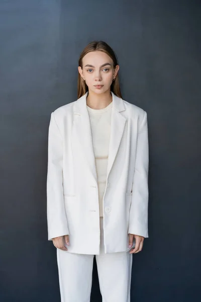 Front view of young woman in white blazer looking at camera on black background — Fotografia de Stock