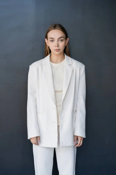 Front view of young woman in white blazer looking at camera on black background — Stock Photo