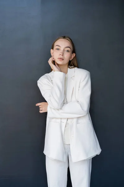 Молода жінка в білому одязі торкається щоки, стоячи на чорному тлі — стокове фото