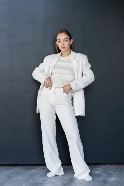 Longitud completa de la mujer en traje blanco y calcetines de pie con las manos en la cintura sobre fondo negro - foto de stock