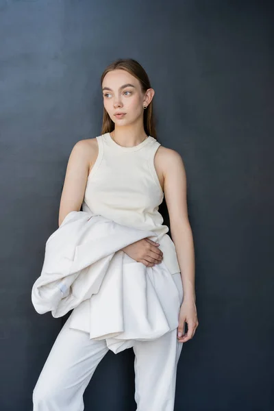 Young woman in white tank top looking away and holding blazer on black background — Fotografia de Stock