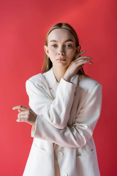 Jovem mulher em blazer branco olhando para a câmera isolada no carmesim — Fotografia de Stock