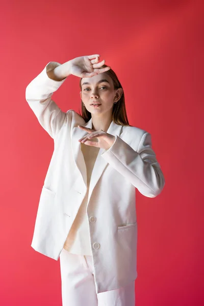 Young and stylish woman in white blazer looking at camera while posing isolated on pink — Fotografia de Stock