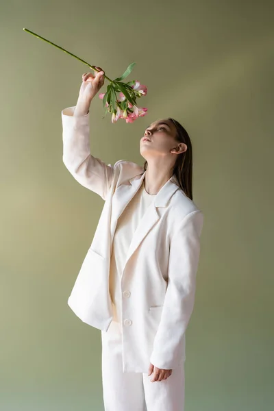 Frau in weißer Kleidung mit Alstroemeriazweig in erhobener Hand isoliert auf grünem Grund — Stockfoto