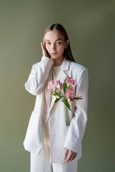 Trendy woman with fresh alstroemeria flowers touching face isolated on green — Stock Photo