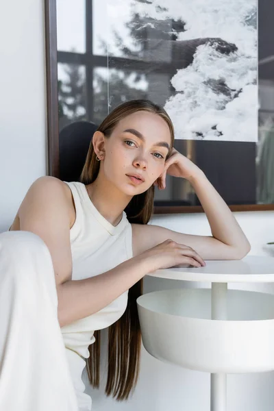 Pretty woman leaning on coffee table near window and looking at camera — Stockfoto