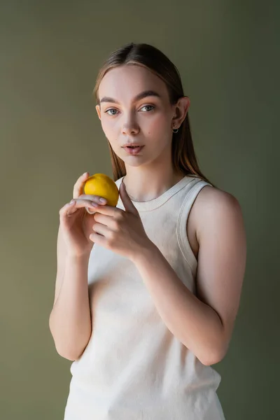 Young woman with ripe lemon looking at camera isolated on green — Stockfoto