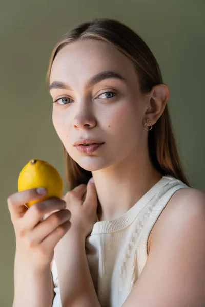 Портрет чарівної жінки зі стиглим лимоном, який дивиться на камеру ізольовано на зеленому — стокове фото