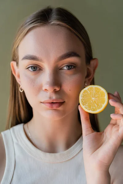 Portrait of pretty young woman showing half of juicy lemon isolated on green — Fotografia de Stock