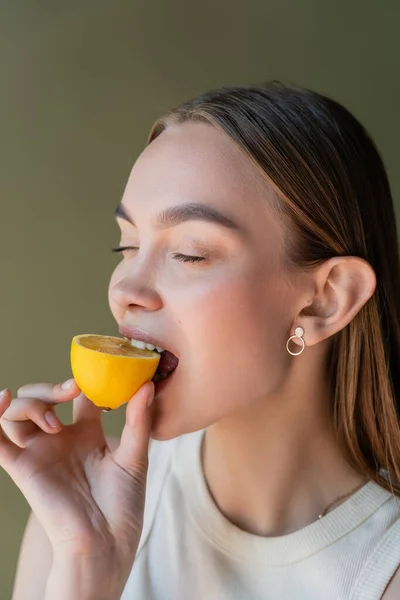 Young woman with closed eyes biting juicy lemon isolated on green — Foto stock