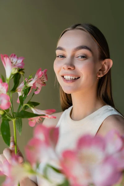 Young and happy woman with pink alstroemeria flowers isolated on green - foto de stock