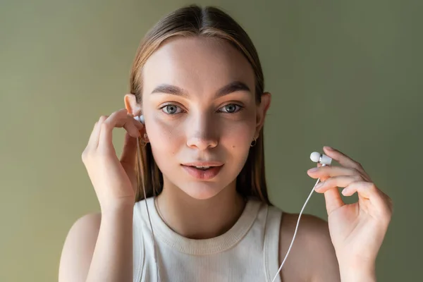Junge Frau mit kabelgebundenen Kopfhörern blickt isoliert auf grüne Kamera — Stockfoto