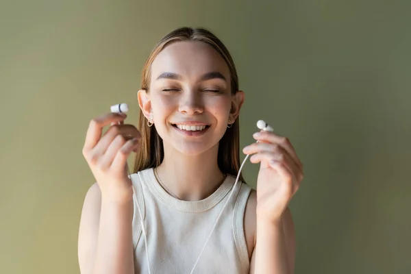 Heureuse jeune femme avec les yeux fermés tenant écouteurs filaires isolés sur vert — Photo de stock