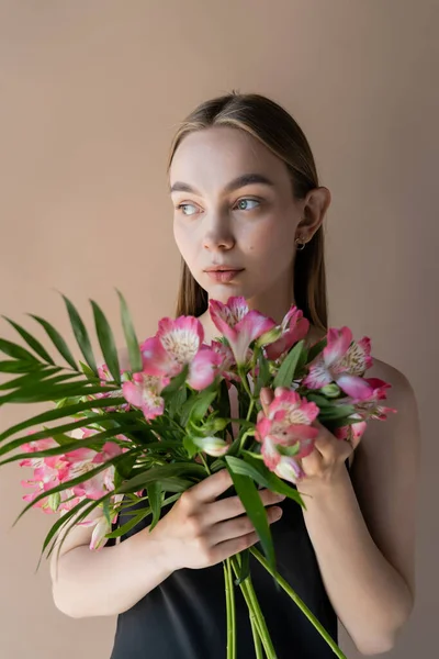 Mulher encantadora com buquê de alstroemeria rosa olhando para longe isolado no bege — Fotografia de Stock