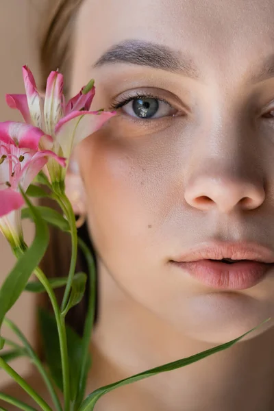 Nahaufnahme Porträt einer gestutzten Frau mit perfekter Haut in der Nähe rosa Alstroemeria-Blüten — Stockfoto