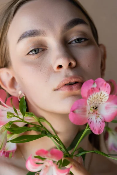 Nahaufnahme Porträt einer sinnlichen Frau mit natürlichem Make-up in der Nähe rosa Blüten isoliert auf beige — Stockfoto