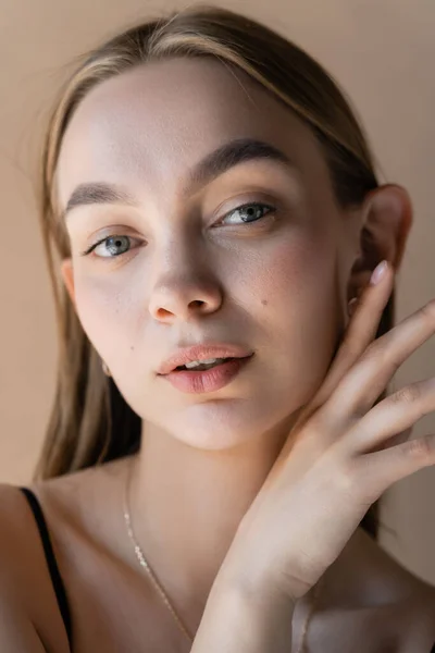 Portrait of woman with natural makeup and hand near perfect face isolated on beige — Photo de stock