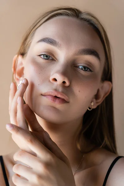 Portrait of charming woman with natural makeup touching perfect face isolated on beige — Stock Photo