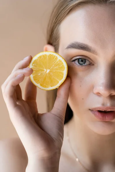 Vue recadrée de la femme avec maquillage naturel tenant moitié citron isolé sur beige — Photo de stock