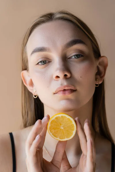 Портрет красивої молодої жінки з ідеальною шкірою, що тримає половину лимона ізольовано на бежевому — стокове фото