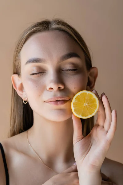 Portrait of pleased woman with closed eyes holding half of juicy lemon isolated on beige - foto de stock