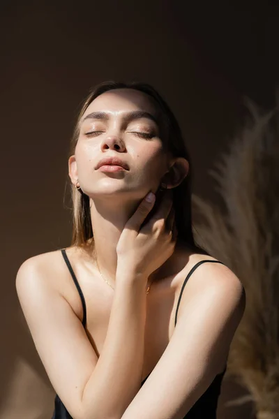 Seductive woman with closed eyes and natural makeup touching neck on dark background — Stock Photo