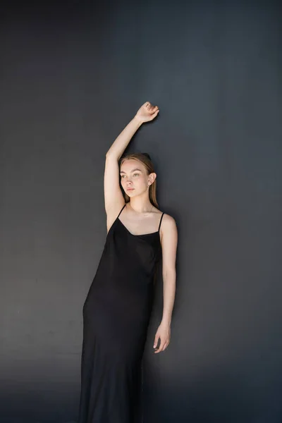 Тонка жінка в сукні ремінця позує з піднятою рукою на чорному тлі — стокове фото