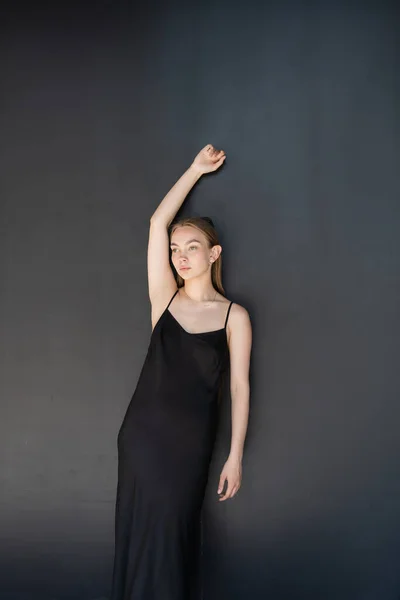 Slim woman in strap dress posing with raised hand on black background — Stock Photo