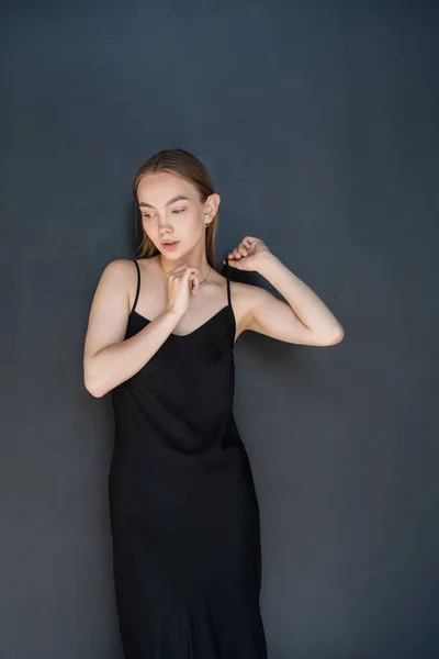 Sensual woman touching strap of black dress on dark background — Foto stock