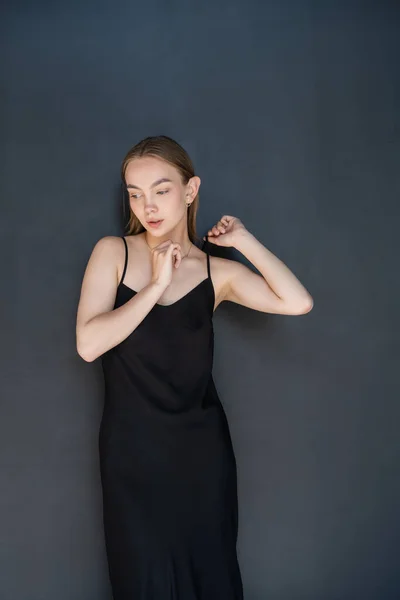 Sensual mujer tocando correa de vestido negro sobre fondo oscuro - foto de stock