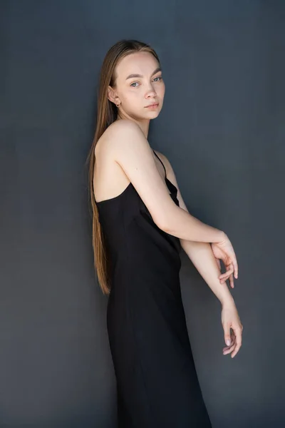 Young long haired woman in strap dress looking at camera on black background — Stockfoto