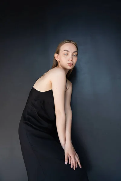 Trendy woman in strap dress looking at camera while posing on black background — Stockfoto