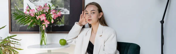 Trendy woman looking at camera near ripe apple and bouquet on coffee table, banner — Stock Photo