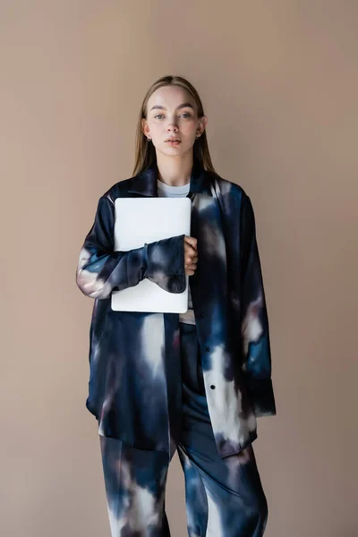 Jeune femme à la mode avec ordinateur portable regardant la caméra isolée sur beige — Photo de stock