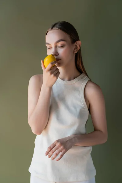 Woman in white tank top smelling aromatic lemon with closed eyes isolated on green — Stockfoto