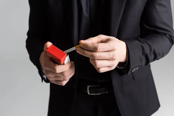 Vista parziale dell'uomo in abito formale nero che tiene il pacchetto di sigarette isolato sul grigio — Foto stock
