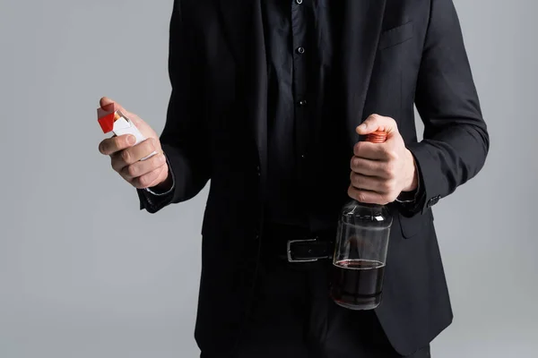 Обрезанный вид человека с пачкой сигарет и бутылкой виски, изолированной на сером — стоковое фото