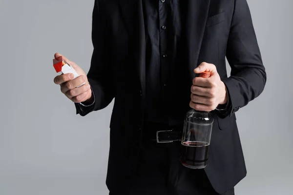 Cropped view of man with cigarette pack and bottle of whiskey isolated on grey — Stock Photo