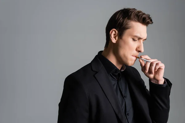 Thoughtful man in black blazer smoking cigarette isolated on grey — Stock Photo